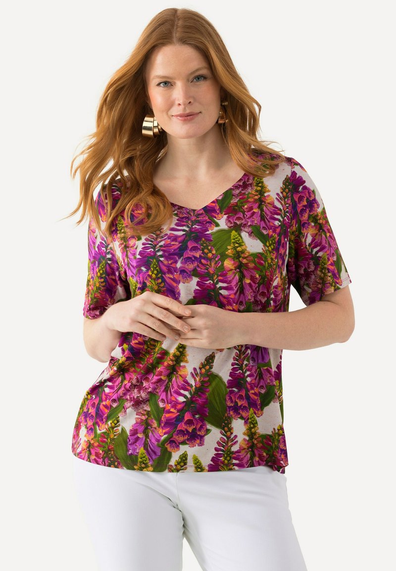 Top de manga corta con escote en V que presenta un patrón floral en tonos de púrpura, rosa y verde sobre un fondo blanco. Fabricado con un tejido suave y liviano.