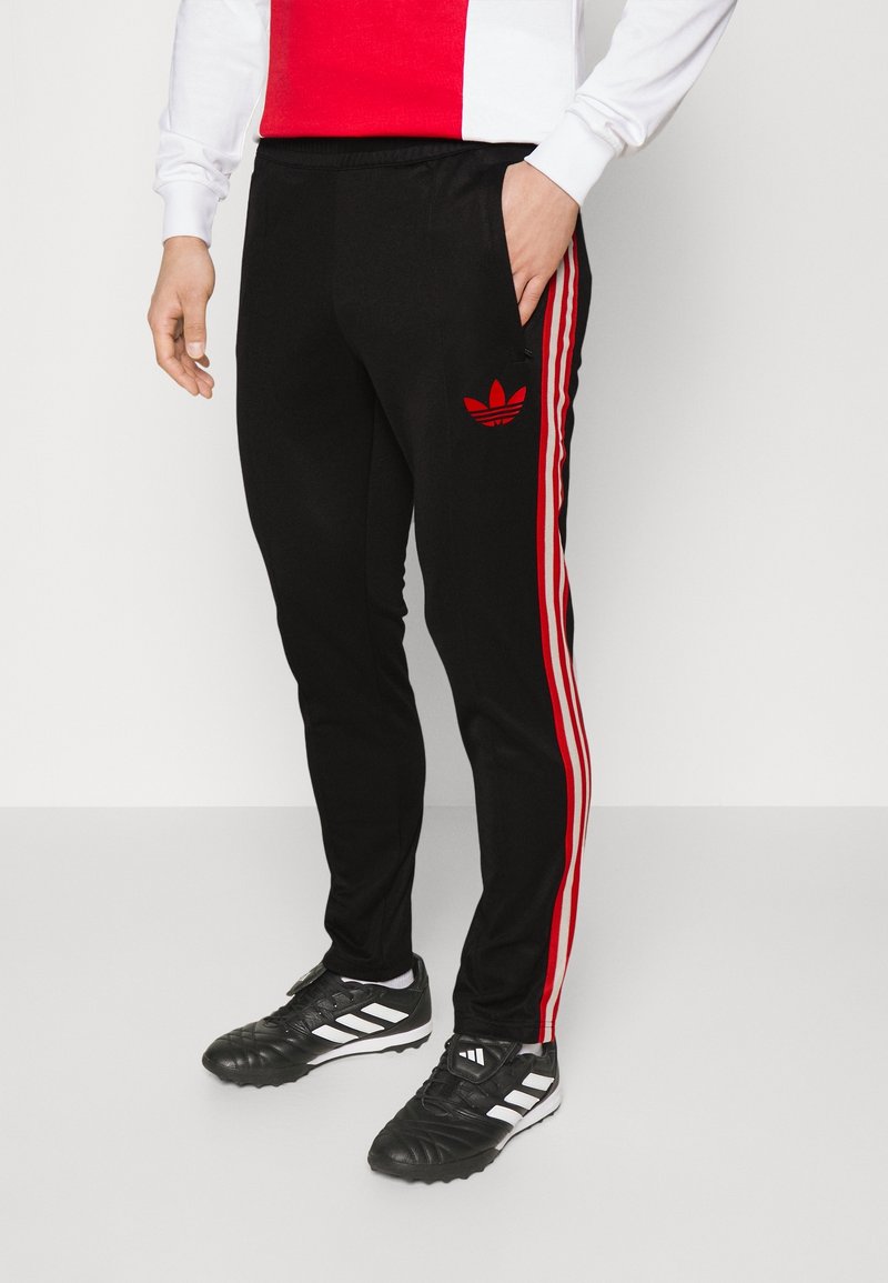 Black athletic pants with red stripes down the sides, featuring an embroidered red adidas logo on the left thigh and side pockets.
