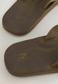 Pruunid nahast sandaalid varbarihmadega, millel on õhuvõtuavad ja talla peal on reljeefsed suurusmärgised.