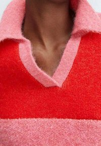 Hals en bovenste borst die een fuzzy coltrui dragen met rood en roze kleurblokken en een V-halsopening.