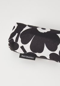 Mustvalge lillemustriga kangast ümara kujuga ümbris. Küljes olev silt kannab nime "marimekko". Sile tekstuur ja pehme materjal.