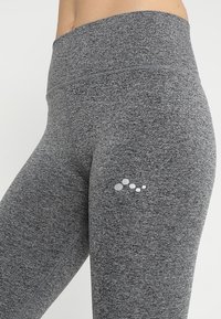 Szare elastyczne legginsy wykonane z teksturowanej tkaniny, z wysokim stanem i małym logo na udzie.