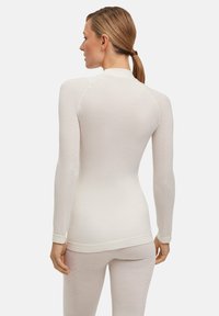 Maglia termica bianca a maniche lunghe con un design aderente, texture a coste e cuciture a contrasto lungo le cuciture, abbinata a leggings bianchi.
