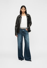 Giacca di pelle nera, top bianco, jeans blu a gamba larga, cintura argento e scarpe nere a punta. Texture lisce con un aspetto casual e stratificato.