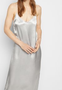 Robe nuisette en soie argentée avec un col en V et de fines bretelles. Texture lisse avec une silhouette fluide, atteignant la mi-longueur.