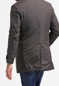 Tmavě šedý prošívaný péřový kabát s rovný střihem, zapínáním na knoflíky na manžetách a hladkou texturou. Vyznačuje se elegantním, minimalistickým designem.