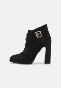 Black suede heeled ankle boots with a rounded toe, side zipper, and decorative gold "B" emblem on the outer side.