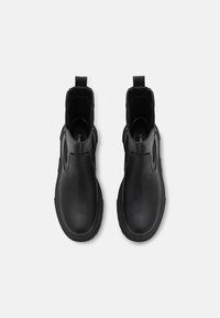 Botas de tobillo de cuero negro con un acabado suave, paneles laterales elásticos y una pestaña en el talón para facilitar el calzado. Suela de goma para agarre.