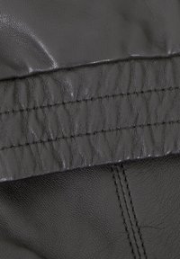 Schwarzes Leder mit strukturierter Oberfläche, das versammelte Abschnitte und sichtbare Nähdetails aufweist. Glatte und leicht glänzende Optik.