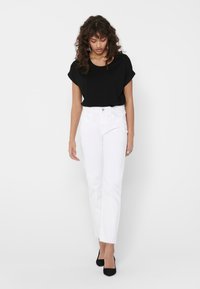 Maglietta nera a maniche corte abbinata a pantaloni bianchi a vita alta con taglio dritto. Il modello indossa tacchi alti neri. Design semplice, senza motivi visibili.