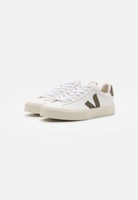 White leather sneakers with beige suede accents and textured rubber sole. Features flat white laces and a subtle logo on the heel.