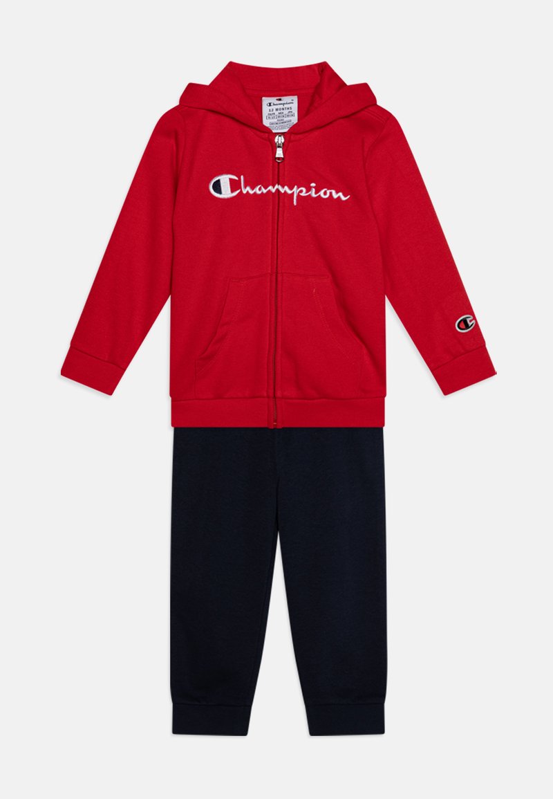 Red zip-up hoodie with white "Champion" logo, paired with navy jogger pants. Hoodie features a front pocket and elastic cuffs.