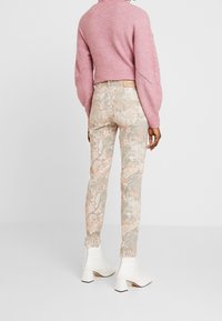 Pantalones ajustados de patrón floral en un beige pálido con acentos verdes y rosas. Suéter de punto rosa oversized y botas blancas hasta el tobillo con tacones cuadrados.