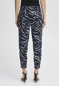 Kalhoty s námořnickým vzorem a zeleným květinovým designem, s elastickým páskem, dvěma zadními kapsami a zúženými kotníky, doplněné černými podpatky.