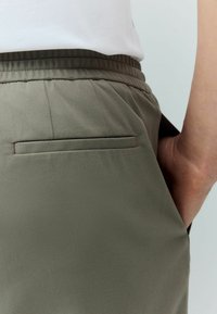 Oleksgreen spodnie o gładkiej strukturze, z płaską tylną kieszenią i elastycznym paskiem dla wygody.