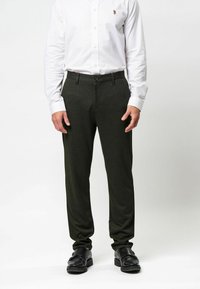 Tamsiai žalios, pritaikytos kelnės, pagamintos iš minkštos medžiagos. Dėlionė su priekinio mygtuko užsegimu ir subtiliomis šoninėmis kišenėmis.