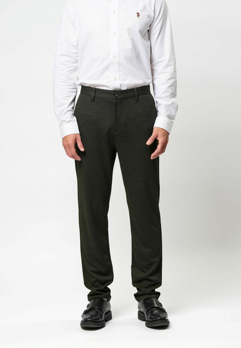 Tamsiai žalios, pritaikytos kelnės, pagamintos iš minkštos medžiagos. Dėlionė su priekinio mygtuko užsegimu ir subtiliomis šoninėmis kišenėmis.