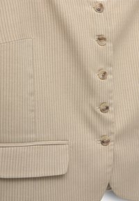 Blazer beige à rayures avec un col à cran, six boutons ronds et une poche plaquée sur le côté gauche. Texture de tissu lisse.