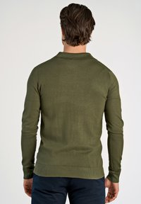 Olivgrüner, taillierter Pullover mit langen Ärmeln, aus strukturiertem Strickstoff gefertigt. Mit Polo-Kragen sowie geripptem Saum und Bündchen.
