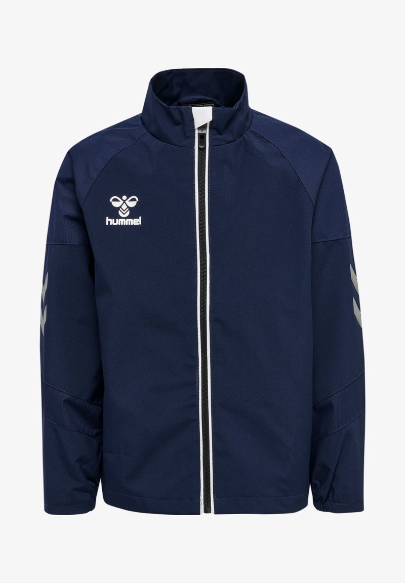Navy windbreaker z wysokim kołnierzem, biały zamek błyskawiczny, logo Hummel na klatce piersiowej i jasnoszare akcenty w zygzaku na rękawach.