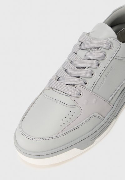 Sneaker en cuir gris avec bout rond, semelle blanche épaisse et lacets texturés. Le panneau latéral a une finition lisse avec des accents minimaux.