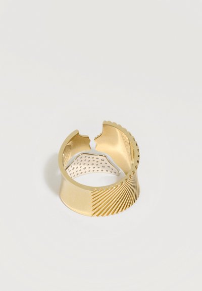 Large bague en or avec extrémités ouvertes, présentant des rainures diagonales d'un côté et une bande intérieure en argent perforée.