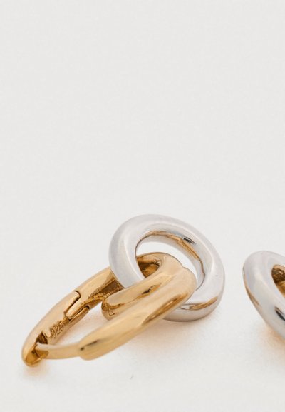 Σκουλαρίκια κρίκοι από χρυσό και ασήμι, με ομαλές, στρογγυλεμένες μορφές, γυαλιστερές επιφάνειες και ελαφρύ σχεδιασμό.