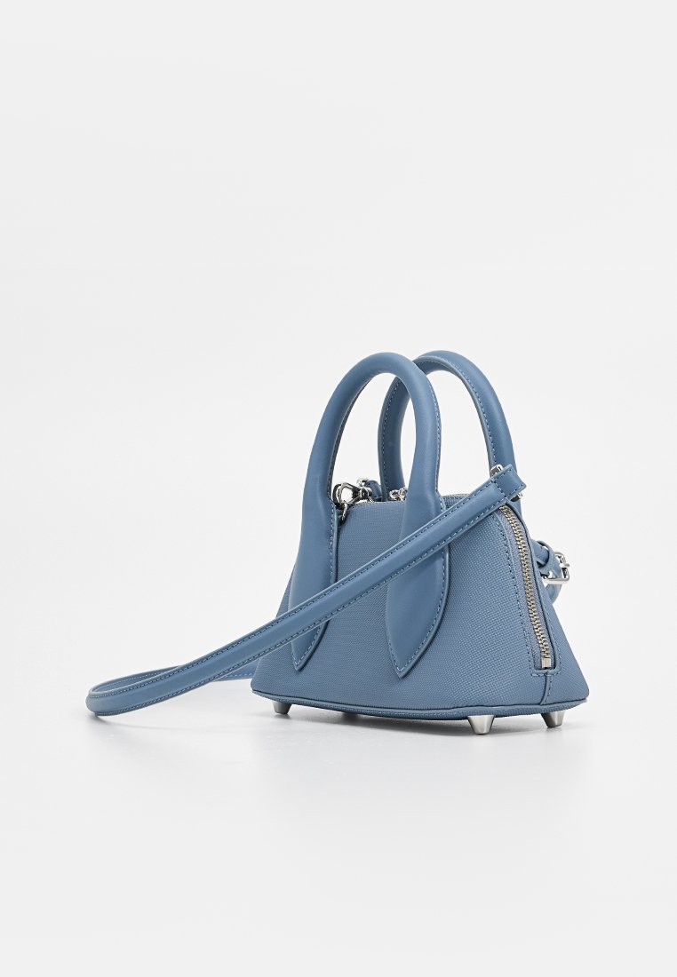 Petit sac à main en cuir bleu avec poignées doubles, longue sangle pour épaule, fermeture éclair et pieds en métal sur fond blanc.