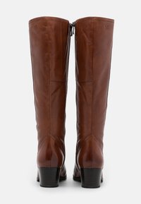 Botas de cuero marrón hasta la rodilla con un acabado suave, cremallera lateral y un tacón bajo apilado. Presentan detalles de costura en la parte trasera.
