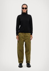 Maglione nero a collo alto con maniche lunghe, abbinato a pantaloni cargo verde oliva con tasche laterali e scarpe chunky nere.
