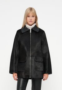 Must musta sarnane karvane mantel läikiva kraega, esine tõmblukuga, kahe suure taskuga ja vaba lõikega, seljaga on kantud heledat kraed.