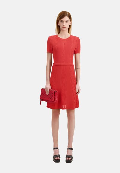 Robe tricotée rouge à manches courtes, avec des motifs texturés, taille ajustée, accompagnée d'une pochette matelassée rouge et de sandales à plateforme noires.