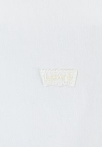 Tessuto bianco con superficie testurizzata, caratterizzato da un logo "Levi's" ricamato beige a forma di etichetta cucita al centro.