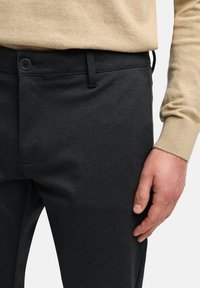 Pantalones negros a medida con una textura suave, un sutil patrón de espiga y un cierre de botón estándar cerca de la cintura.