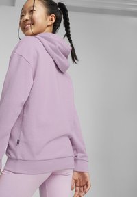 Sudadera de algodón morada con capucha, puños y dobladillo acanalados. La tela parece suave con una textura lisa, llevada con leggings a juego.