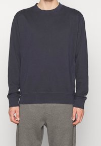 Mörkblå sweatshirt i ett mjukt tyg; har rundad halsringning, ribbade ärmslut och en liten tonal logotyp på bröstet. Matchas med gråa sweatpants.