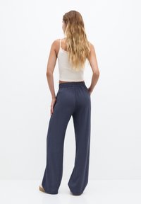 Marineblauwe wijde pantalons van een textuurstof met een elastische tailleband. Gepaard met een beige tanktop, voorzien van dunne bandjes en kantafwerking.