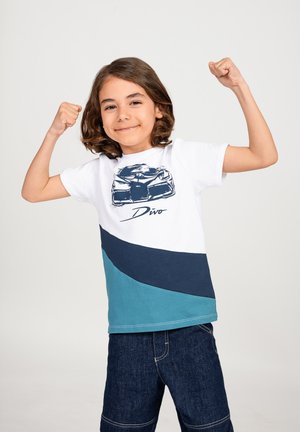 T-shirt per bambini con blocchi di colore bianco, blu navy e teal. Grafica frontale di un'auto con il testo "Divo" sottostante. Maniche corte, collo rotondo.