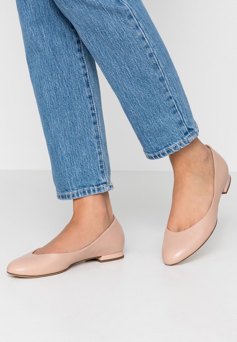 Ballerines en cuir beige avec un bout rond et un petit talon, associées à un jean en denim bleu clair, sur fond blanc.