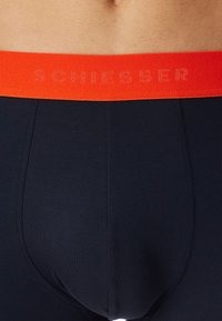 Boxer da uomo blu navy con un vivace elastico arancione recante il testo "SCHIESSER". Il tessuto appare liscio e aderente.