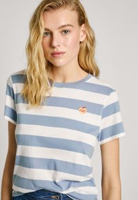 T-shirt rayé bleu et blanc en coton doux, avec un col rond et un petit logo orange brodé sur la poitrine.
