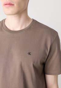 Braunes T-Shirt mit kurzen Ärmeln aus weichem Stoff, mit Rundhalsausschnitt und einem kleinen schwarzen "CK"-Logo auf der Brust.