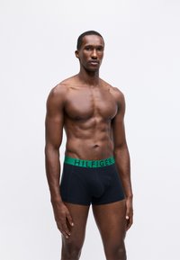Fekete boxer short zöld "HILFIGER" derékkal, kényelmes fazonnal és sima tapintással, izmos felépítésű férfi modellen.