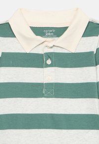 Groen en crèmekleurig gestreepte polo met een kraag, voorzien van drie knopen en een zachte katoenen textuur. Merktag zichtbaar aan de binnenkant.