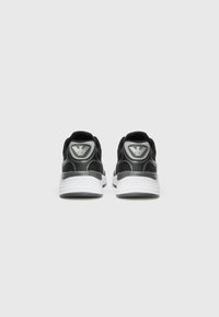Black athletic shoes with a mesh upper, joined by a white midsole. Features a logo accent on the heel and a textured design.