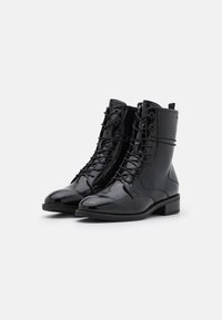 Botas de piel negras hasta el tobillo con acabado de charol brillante, cierre de cordones, puntera redonda y tacón bajo en bloque. La parte delantera presenta detalles de panel texturizado.