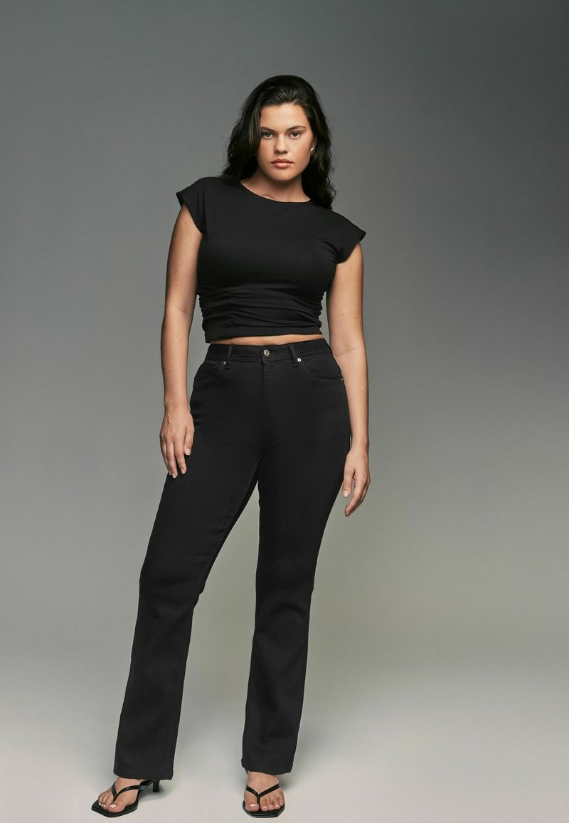 Zwart cropped t-shirt met capmouwtjes, gecombineerd met hoge taille zwarte jeans. Glad textuur, aansluitende stijl. Zwarte sandalen met bandjes maken de look compleet.