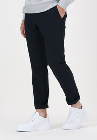 Black, rolled-cuff pants made of soft fabric, paired with white sneakers featuring a textured side design and lace-up closure.