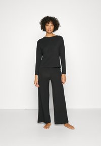 Zwart loungewear set met een langemouwen top en wijde broek, gemaakt van zachte stof met een relaxte pasvorm. Geen patronen of accenten.
