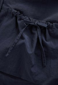 Navy tyg med en strukturerad yta som har en dragsko i midjan och en samlad design för justerbar passform.